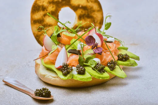 BAGEL WITH AVOCADO, BLACK GARLIC, AND SALMON TOPPED WITH CELESTE CAVIAR